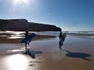 Two surfgirls walking with surfboards over an empty beach at zavial